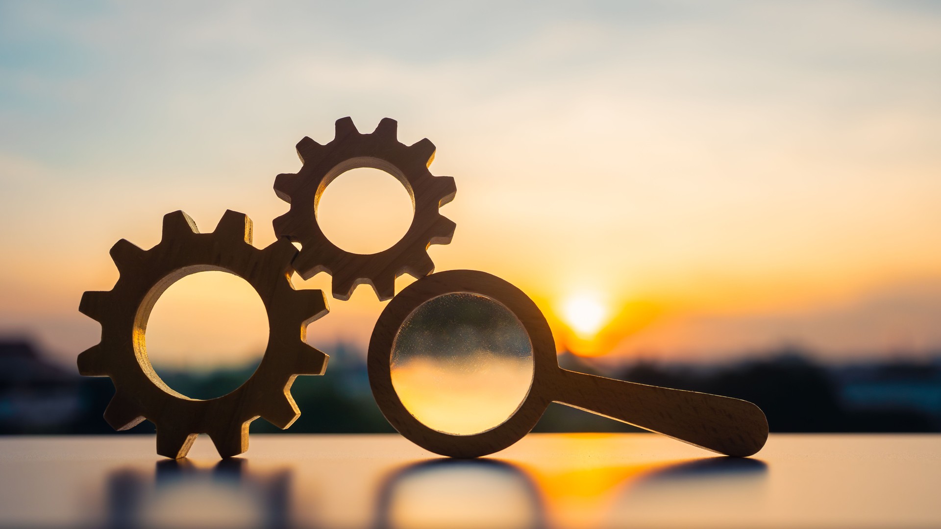 Symbol of gears and magnifying glass placed on table during sunset concept of finding good system for benefit in organization or work system.