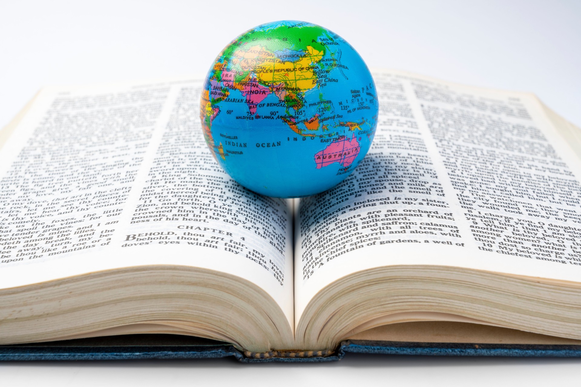 Opened book of Holy Bible with globe. It is laying on white background. Symbol of faith and worship in God